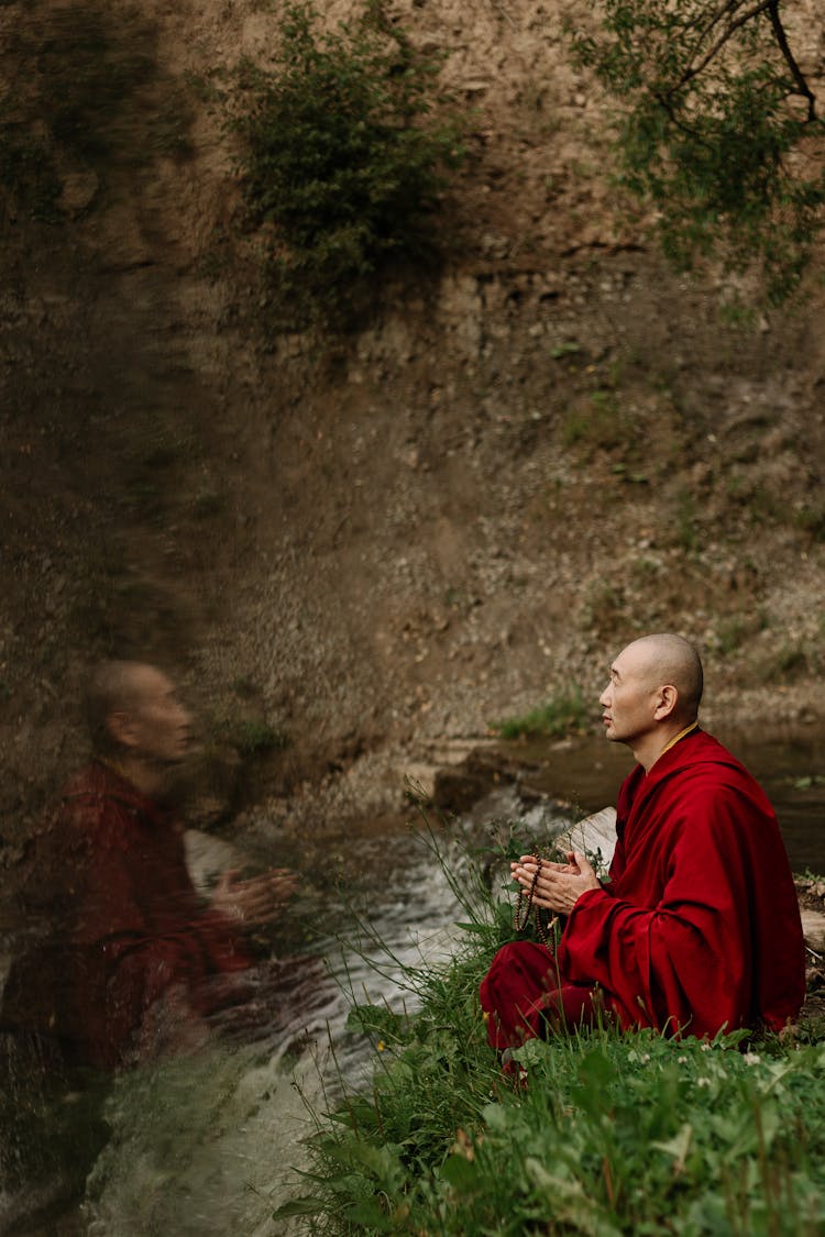 Monk Meditating In Yoga Position Sitting On A Grass