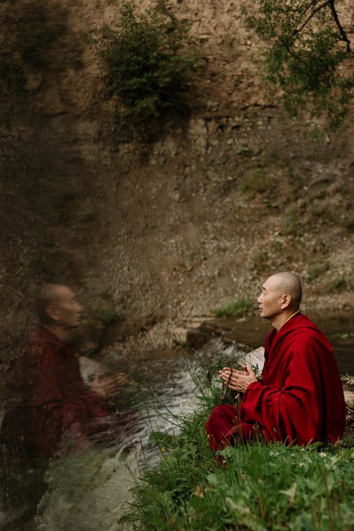 Free A serene view of a Buddhist monk meditating beside a tranquil river, reflecting in prayer. Stock Photo