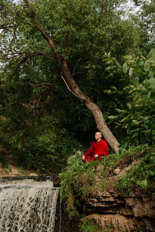 Free Tranquil scene of a monk meditating by a lush waterfall surrounded by greenery. Stock Photo