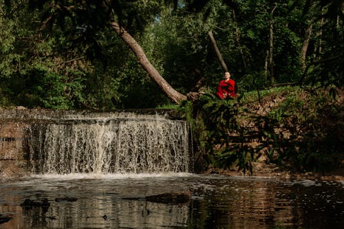 Person in Red Jacket Sitting on Rock Near Water Falls