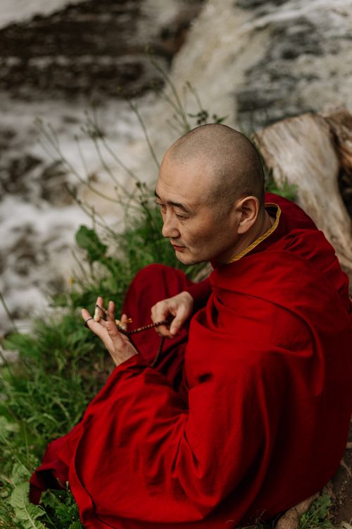 Free Serene image of a Buddhist monk in meditation by a flowing river, holding prayer beads. Stock Photo