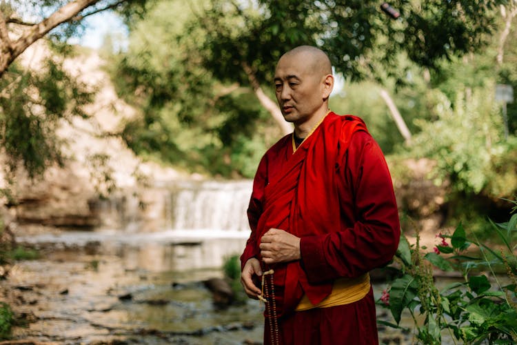 Monk In Red Robe Standing On A Park Holding A Prayer Beads