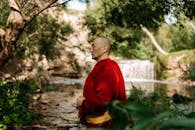 在郁郁葱葱的热带环境中，身着红衣的僧人正于宁静的瀑布旁冥想