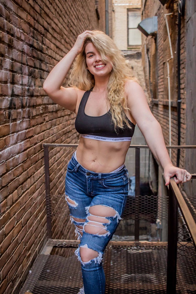 Stylish Smiling Woman In Modern Ripped Jeans On Balcony