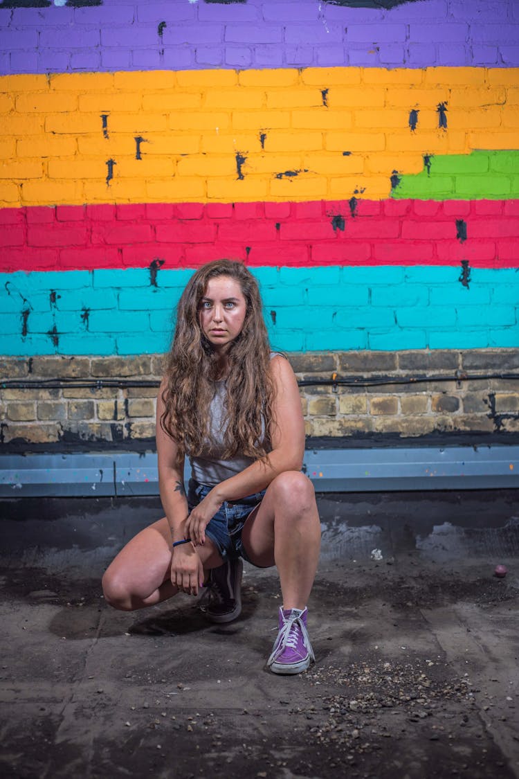 Woman Crouching In Front Of A Wall With A Rainbow Graffiti 