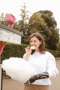 Smiling woman with prosthetic arm enjoying cotton candy outdoors in summer.