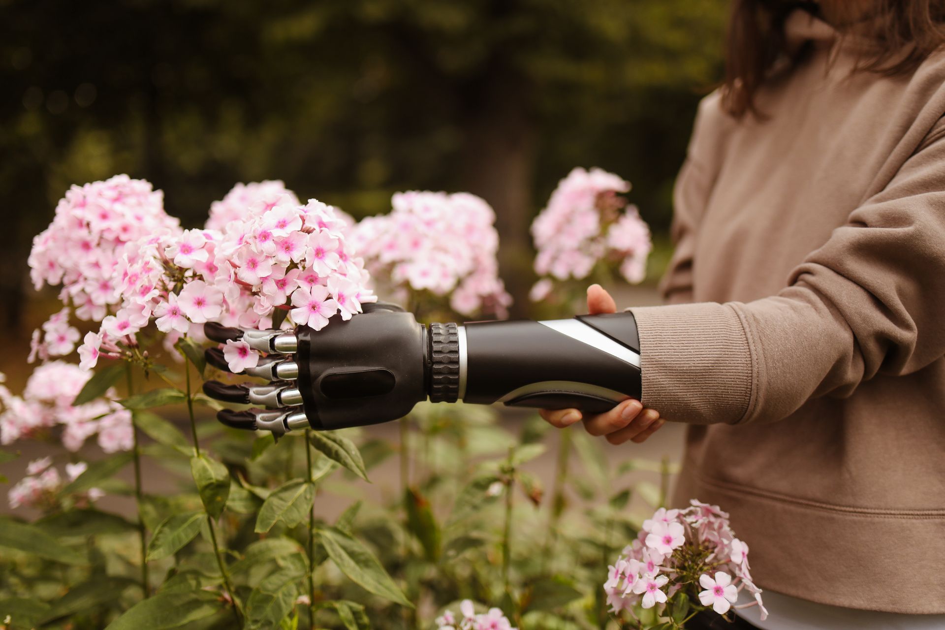 A prosthetic arm admires pink flowers in a serene garden setting.