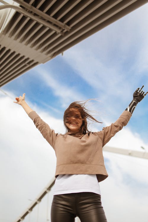 Woman in Brown Long Sleeve Shirt and Black Pants Raising Her Hands