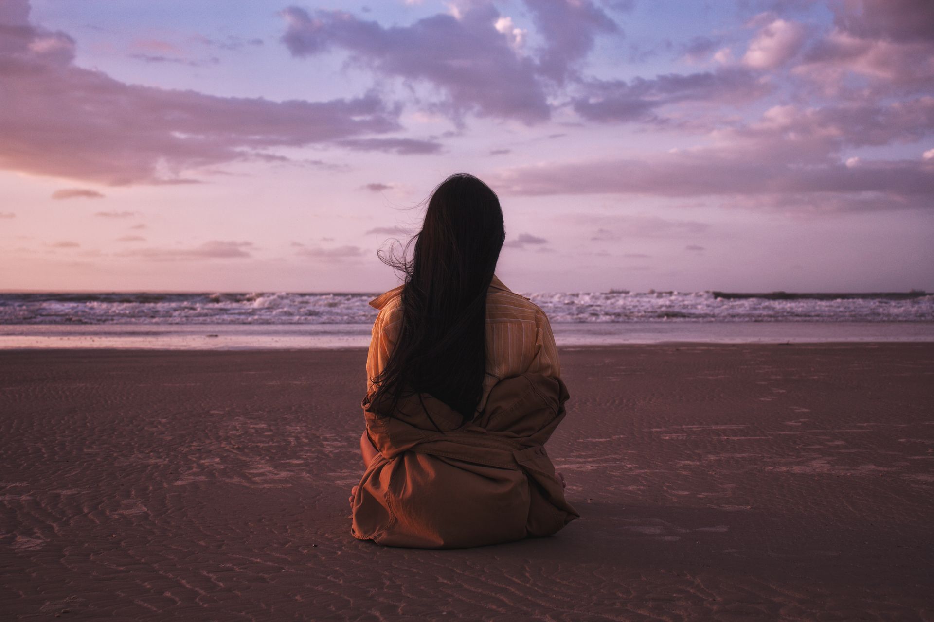 Woman sitting alone on a Brasil beach at sunset, embracing the tranquil seaside view.