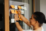 Woman Writing on Sticky Note on Window