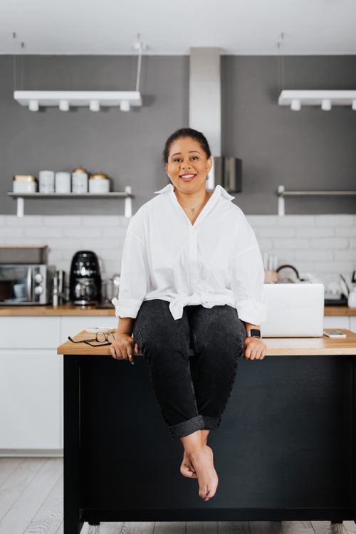 Free A woman smiles while sitting on a modern kitchen countertop in a contemporary styled room. Stock Photo