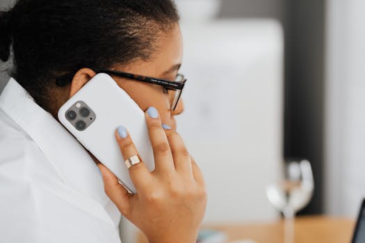 Black woman with eyeglasses using phone, captures focused communication moment.