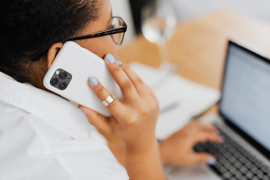 A woman multitasking with a smartphone and laptop in an office setting, showcasing modern technology use.