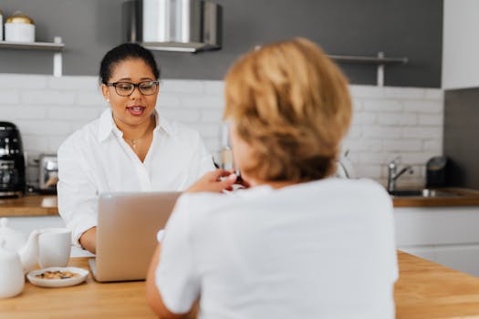 两个女人在现代化的厨房里一起交谈，并使用着笔记本电脑