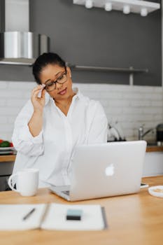 Black woman in white shirt using a laptop in a home office setting.