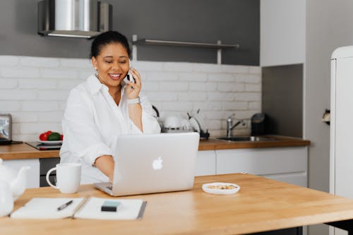 Free Woman in White Dress Shirt Talking on the Cellphone while Using a Laptop Stock Photo