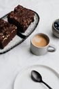 Chocolate Cake on White and Black Ceramic Plate Beside White Ceramic Mug With Brown Liquid