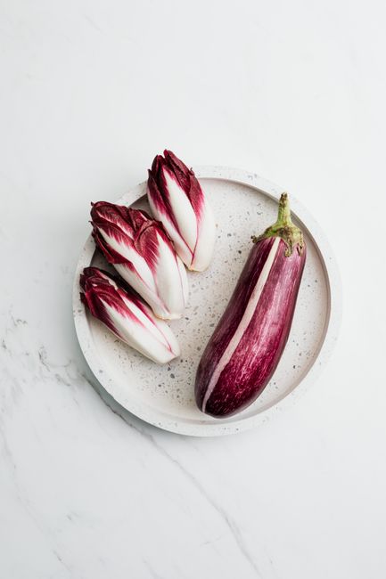 A top-down view of a striped eggplant and red Belgian endive on a speckled ceramic plate.