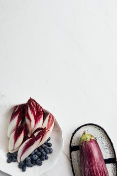 Top view of sliced radicchio, eggplant, and blueberries on white background.