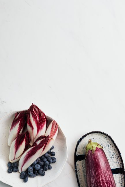 A halved head of radicchio showing its tight magenta and white leaves next to a few loose shredded leaves on a wood board.