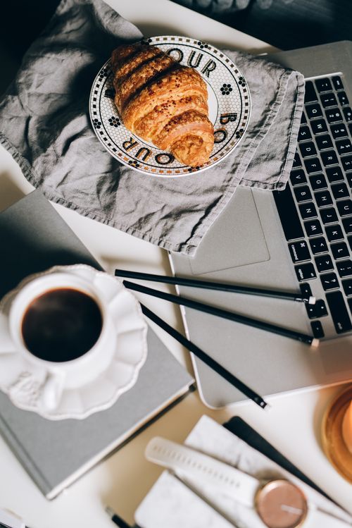 Free Stylish workspace with a laptop, coffee, and croissant on a table. Perfect for work-from-home inspiration. Stock Photo