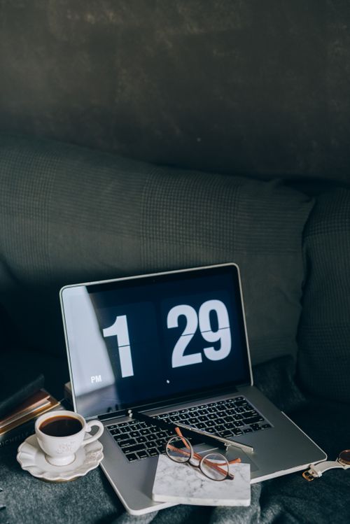 Free A cozy indoor workspace featuring a laptop, coffee cup, and eyeglasses on a couch. Stock Photo