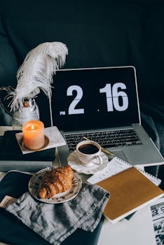 A peaceful work-from-home desk featuring coffee, croissant, candlelight, and a laptop.