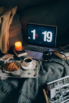 A relaxing evening setup with coffee, croissant, and candle beside a laptop displaying time.