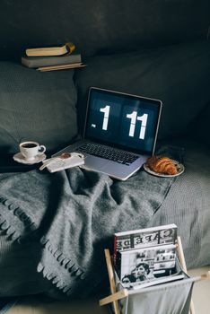 Relaxing home workspace with a laptop, coffee, and croissant on a cozy sofa. Perfect morning setup.