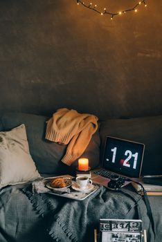 A cozy setup with a laptop, croissant, and coffee cup on a bed illuminated by warm lighting.