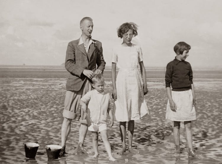 Grayscale Photo Of A Family Standing On The Beach 