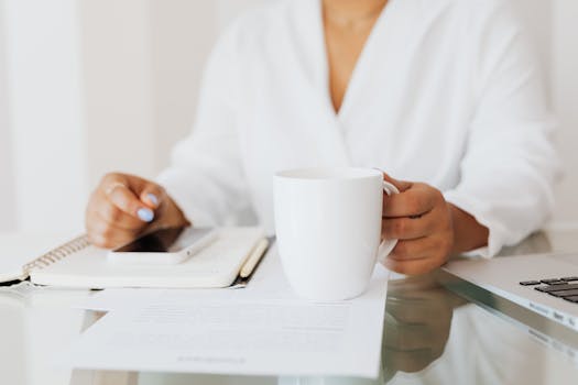 Woman holding a white mug at a desk with documents and laptop in an office.