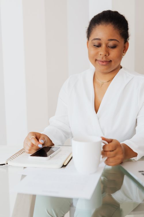 Free An African American woman enjoys a quiet moment with coffee at a modern office desk. Stock Photo