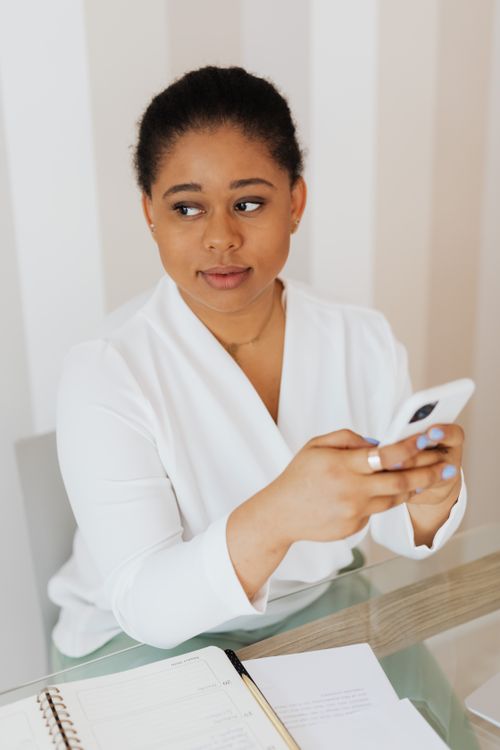 Free A woman holding a smartphone while seated indoors, wearing a white top. Stock Photo