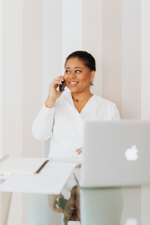 Free Smiling woman using smartphone at desk with laptop in modern office. Stock Photo