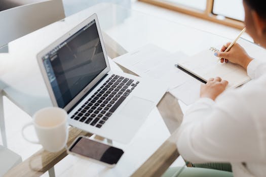 在玻璃桌前工作的人，手里拿着笔记本电脑和咖啡杯