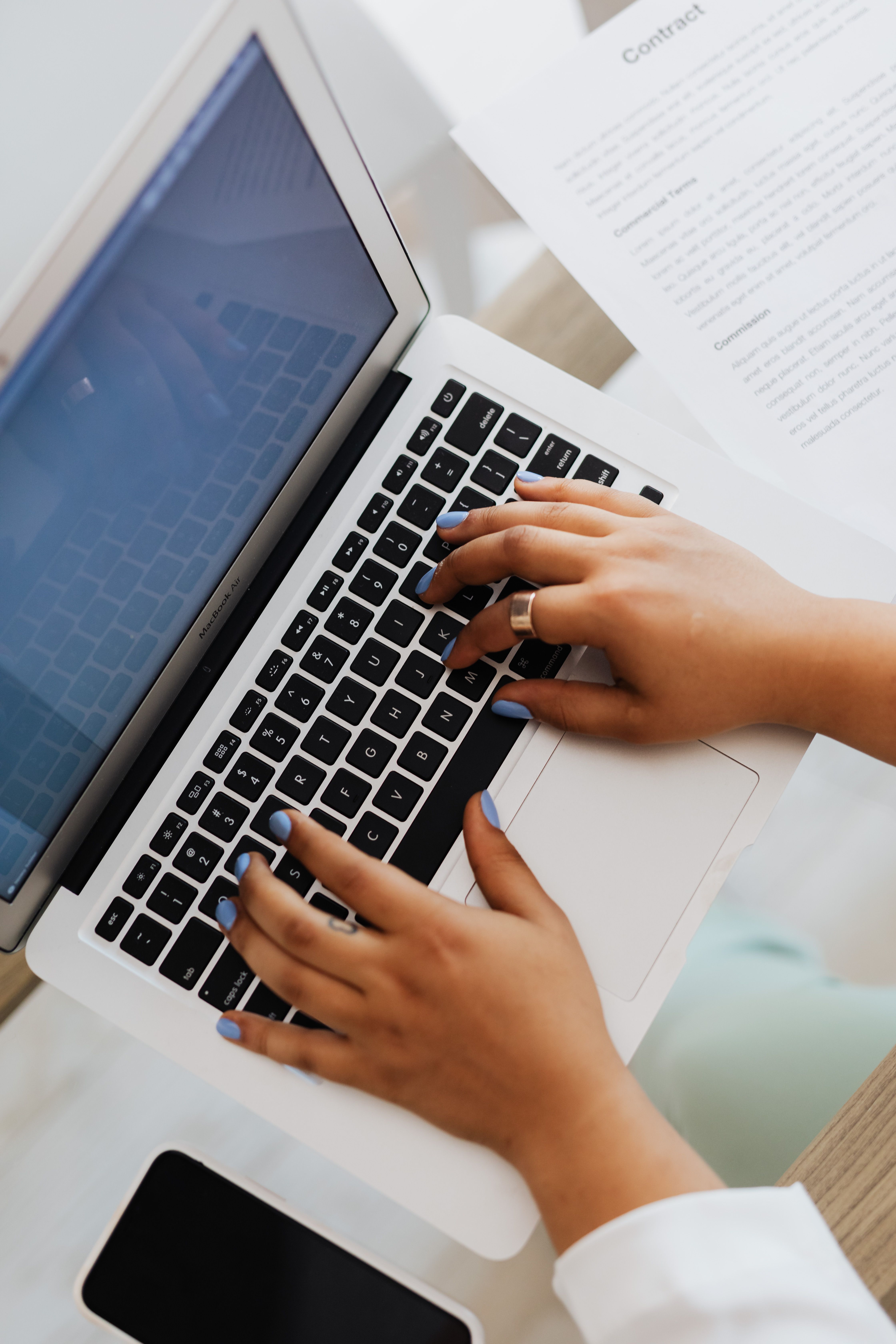 Primo piano di mani che digitano su un laptop moderno in uno spazio di lavoro con documenti.