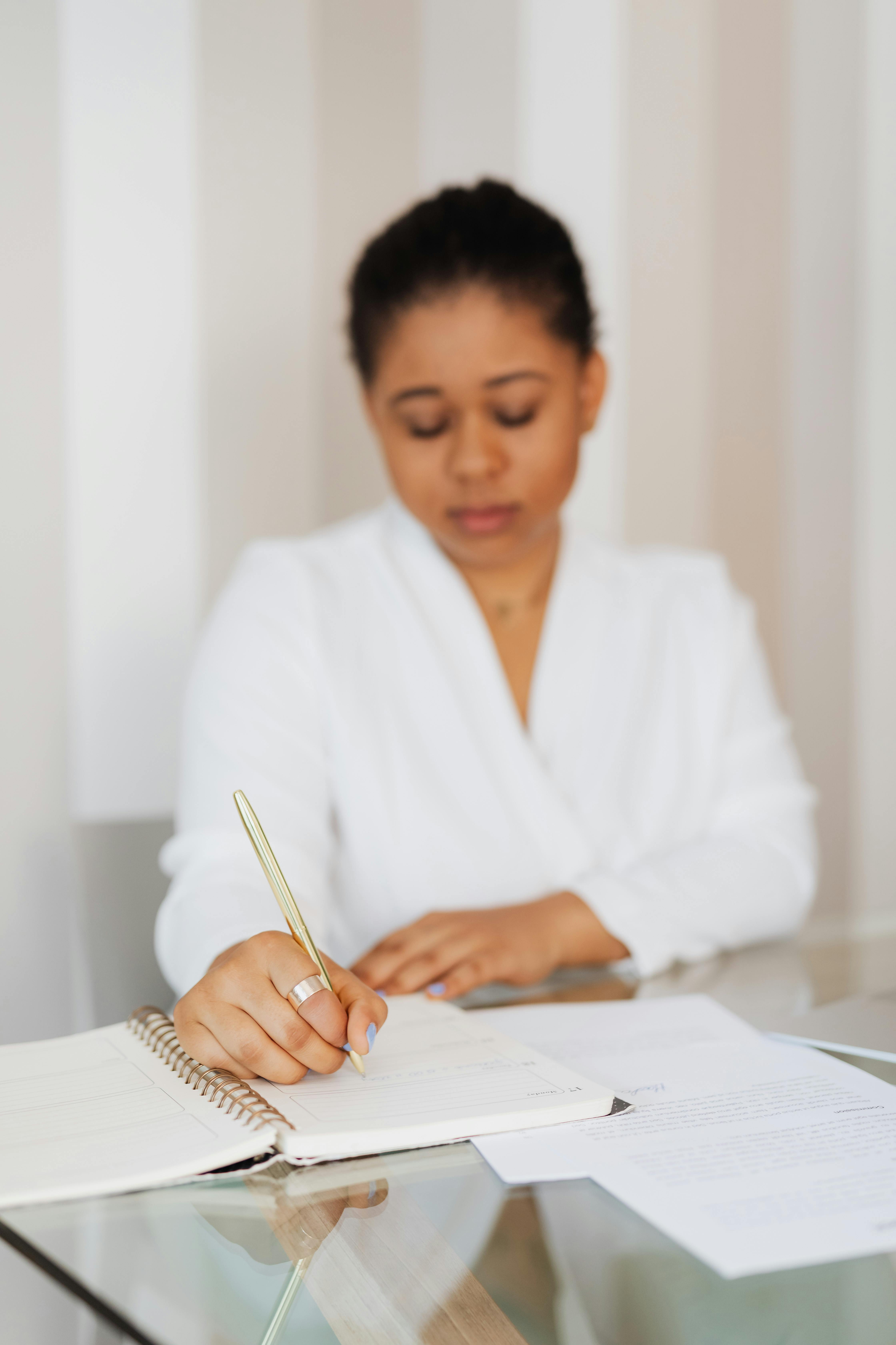 一位穿着白色衣服的黑人妇女正在室内专注地写笔记