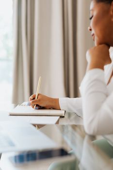 一名妇女坐在室内，用笔在笔记本上记笔记，陷入沉思