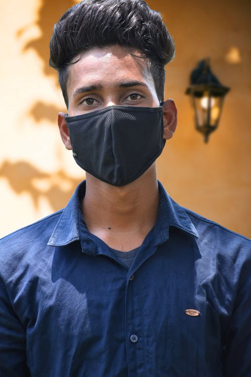 Free Portrait of a young man wearing a face mask and blue shirt standing outside with a warm background. Stock Photo