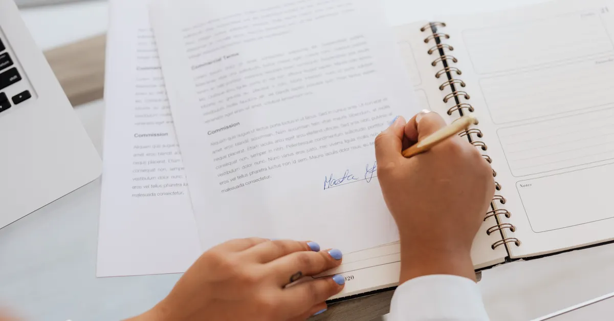 Hands signing a contract on a desk, symbolising a negotiated legal agreement