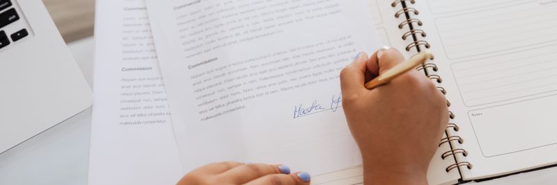 Close-up of hands signing a contract on a desk with office supplies, symbolizing legal agreements.