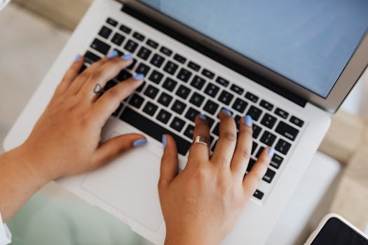 Hands with painted nails typing on a laptop, depicting modern technology.