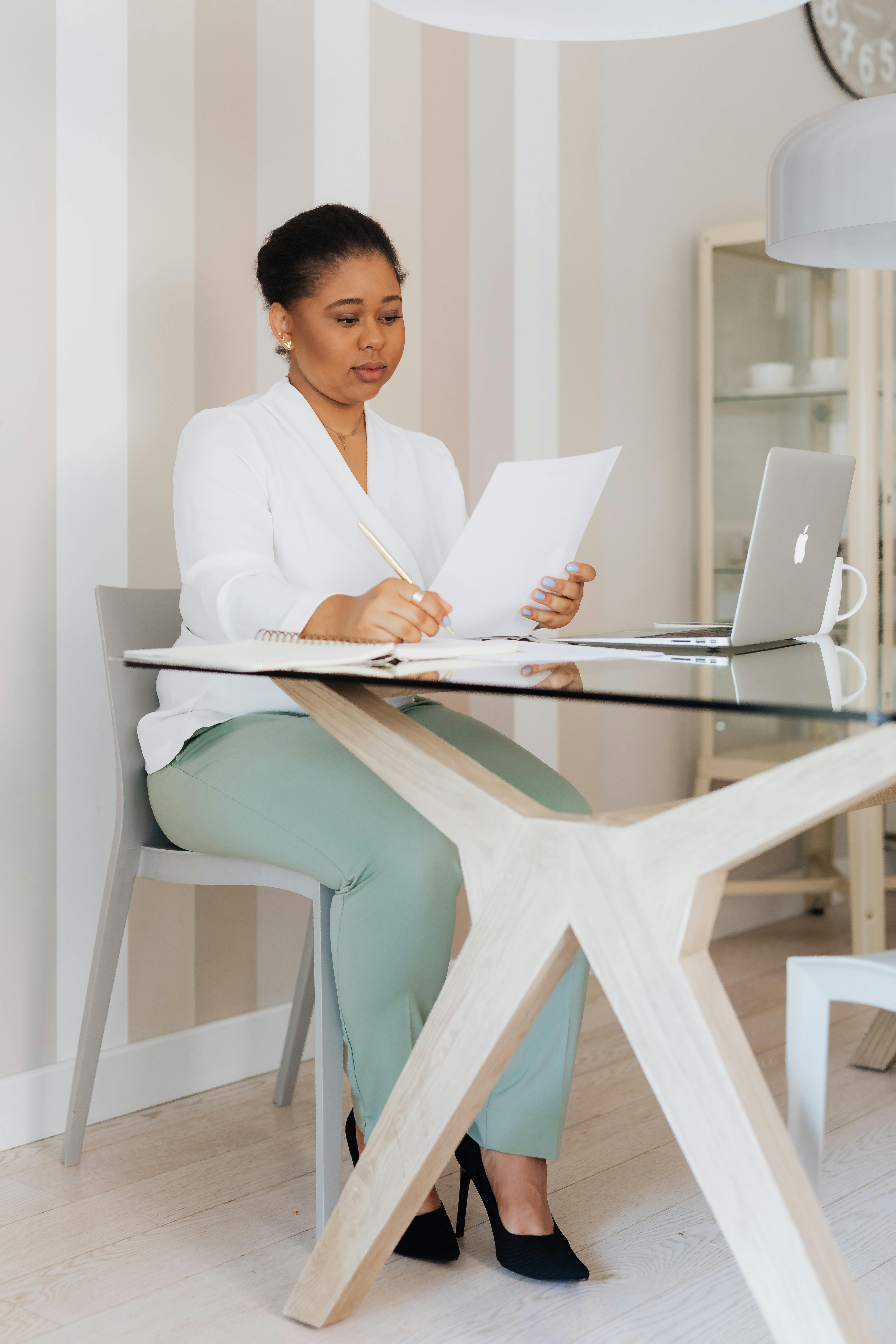 woman in white top sitting on a chair while reading a document