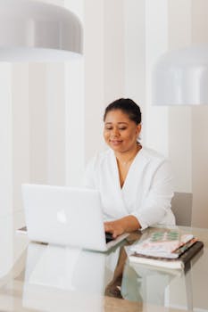Confident woman using a laptop in a bright, modern office setting.