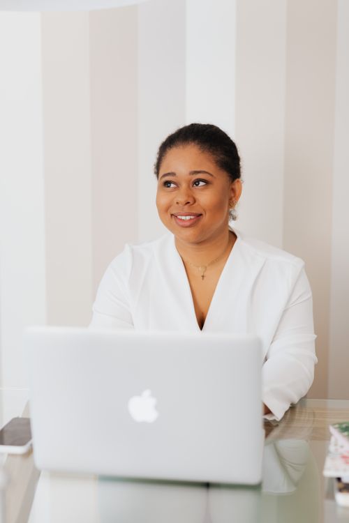 Free Smiling woman in a white top using a laptop in a modern, bright office setting. Stock Photo