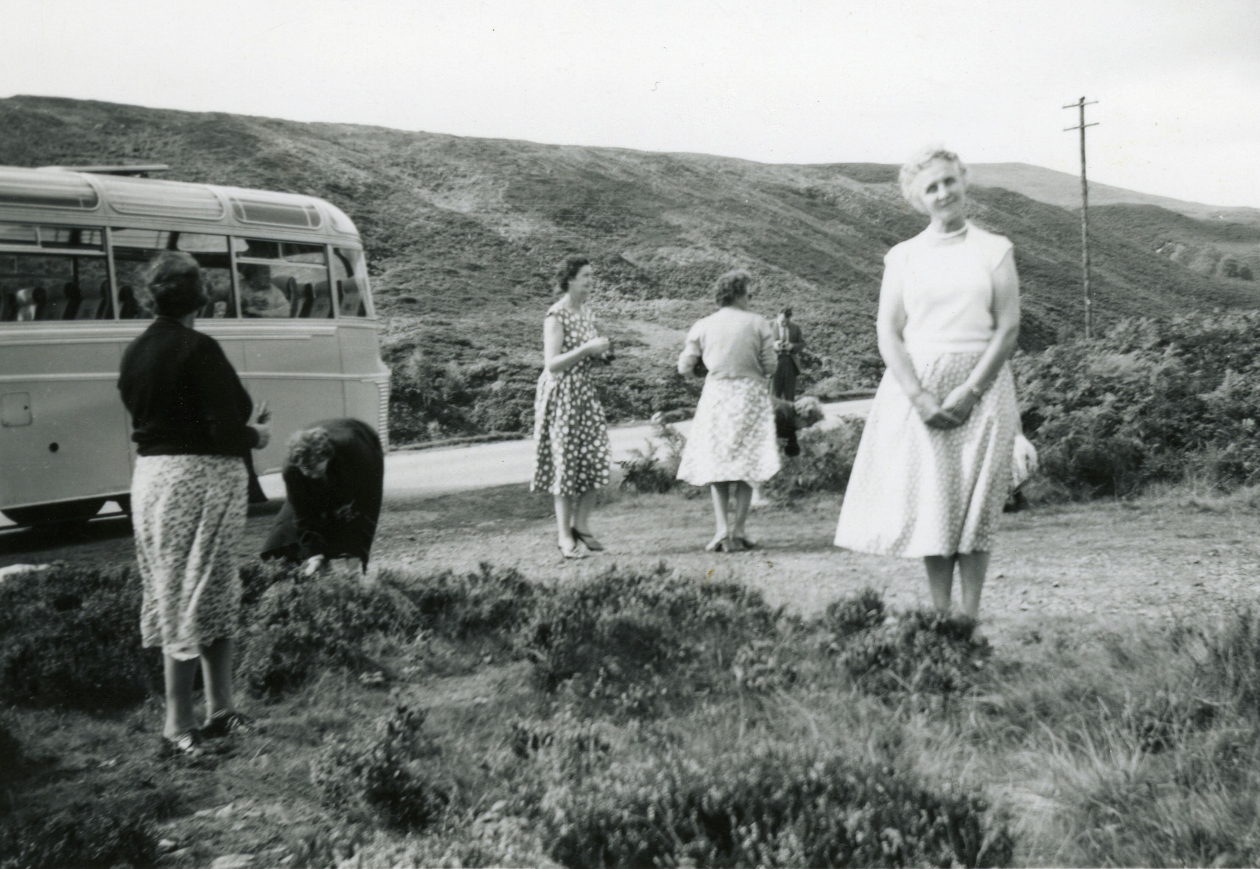 Black-and-white photo of women near a bus in a rural landscape.