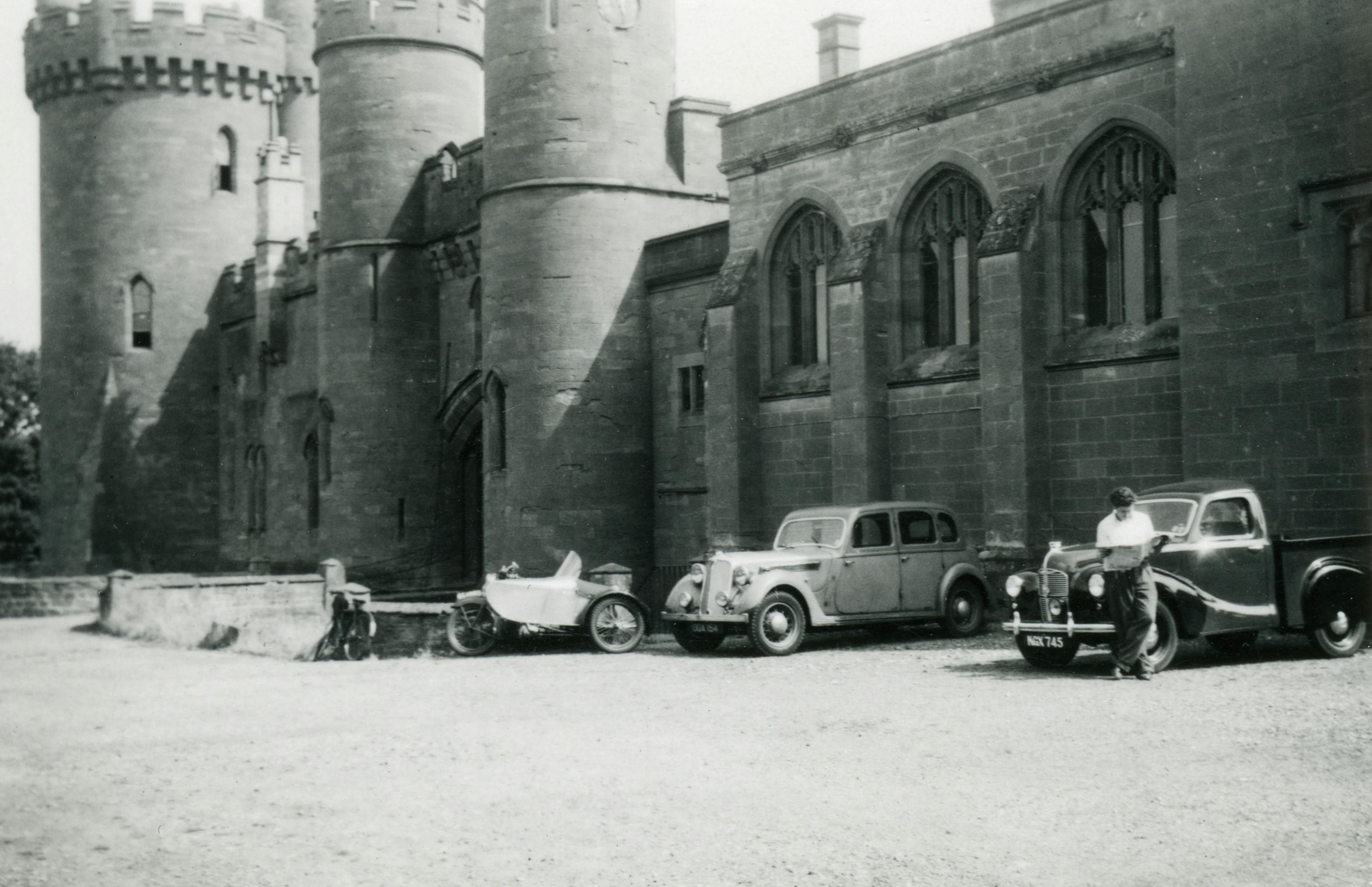 A timeless black-and-white photo of classic cars parked by a historic castle.