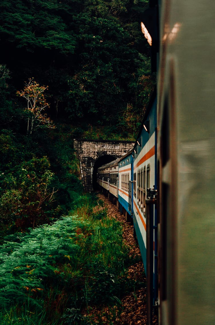 Old Train Driving On Railroad Against Green Trees