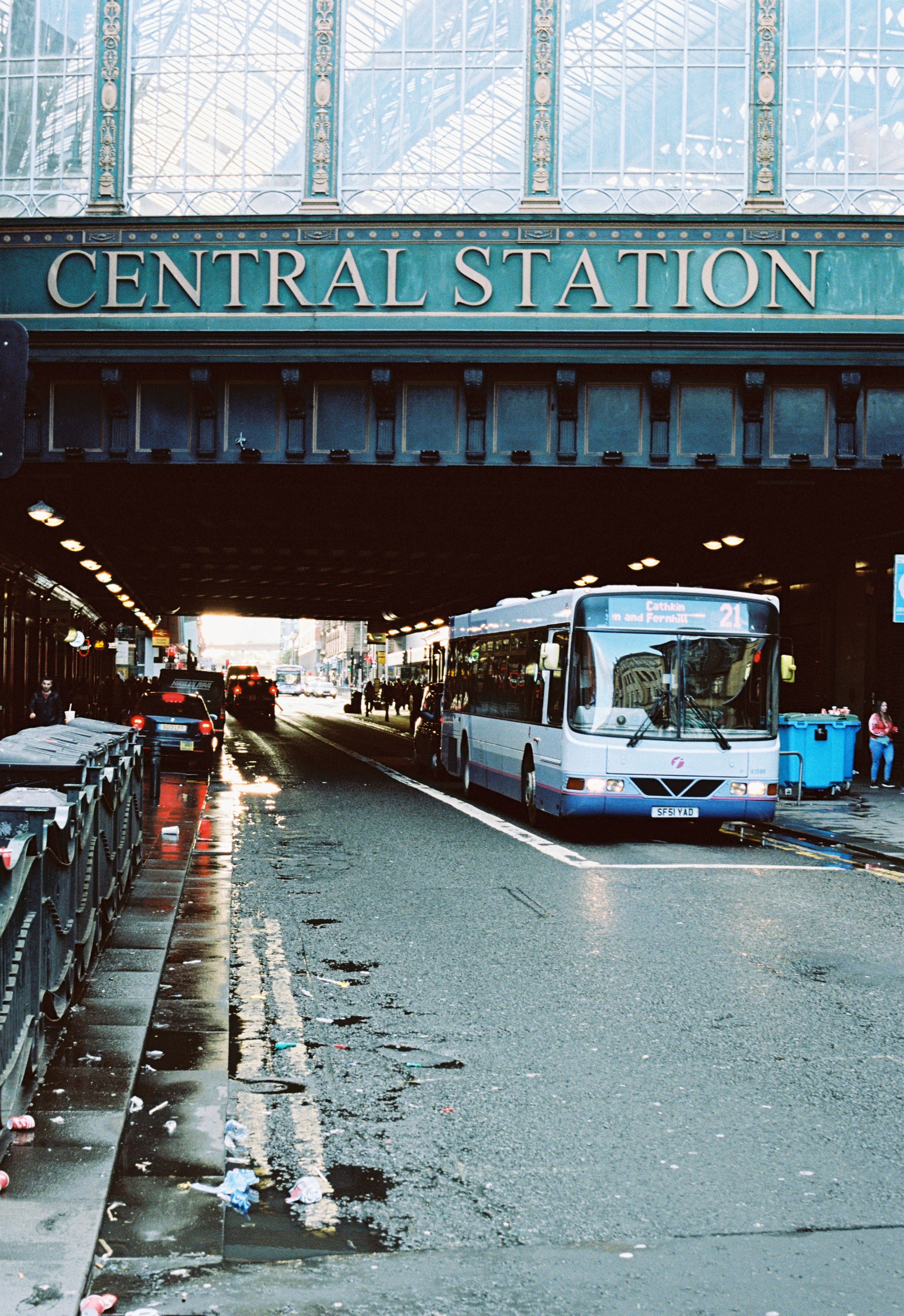 Street view of a bus passing under Glasgow's Central Station on a city road.